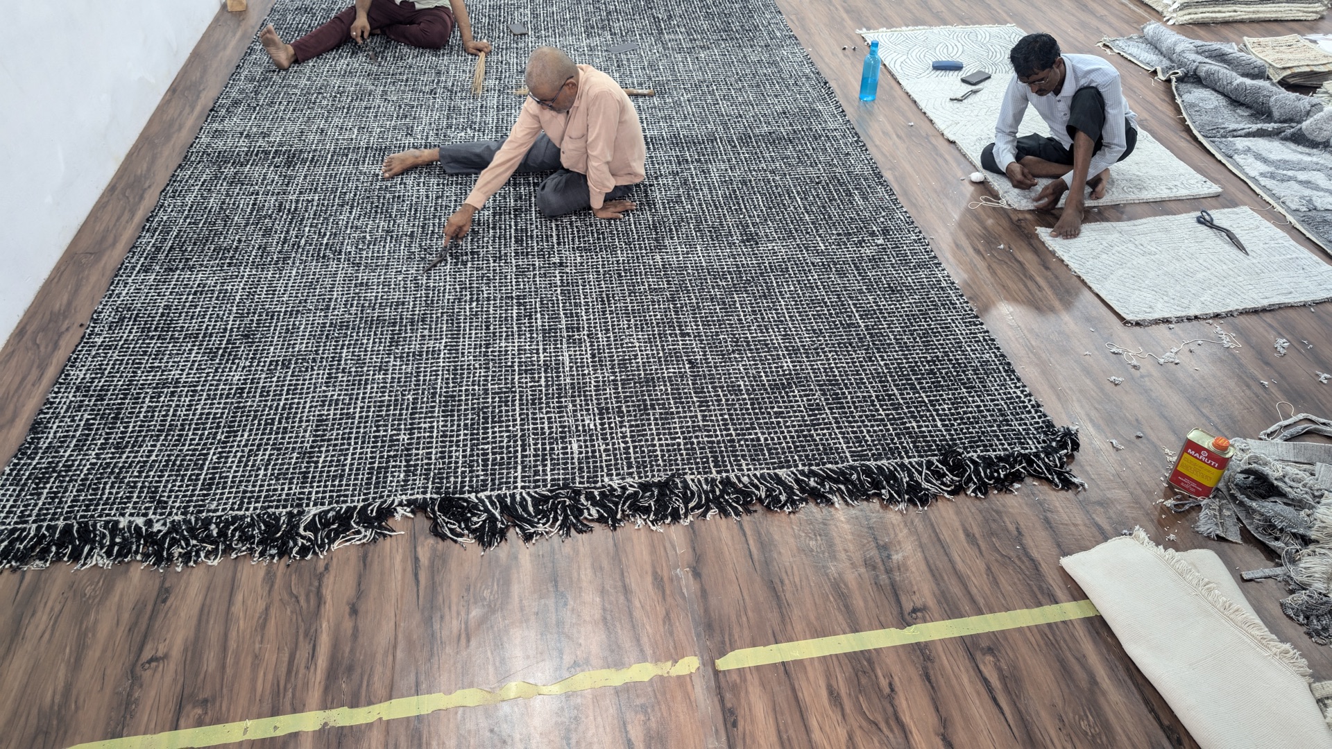 Three artisans completing a large black and ivory custom rug in the Bhadohi workshop